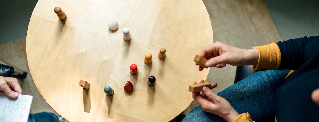 Ein Tisch in der Vogelperspektive, zwei Menschen sitzen sich gegenüber und Spielfiguren stehen auf dem Tisch.
